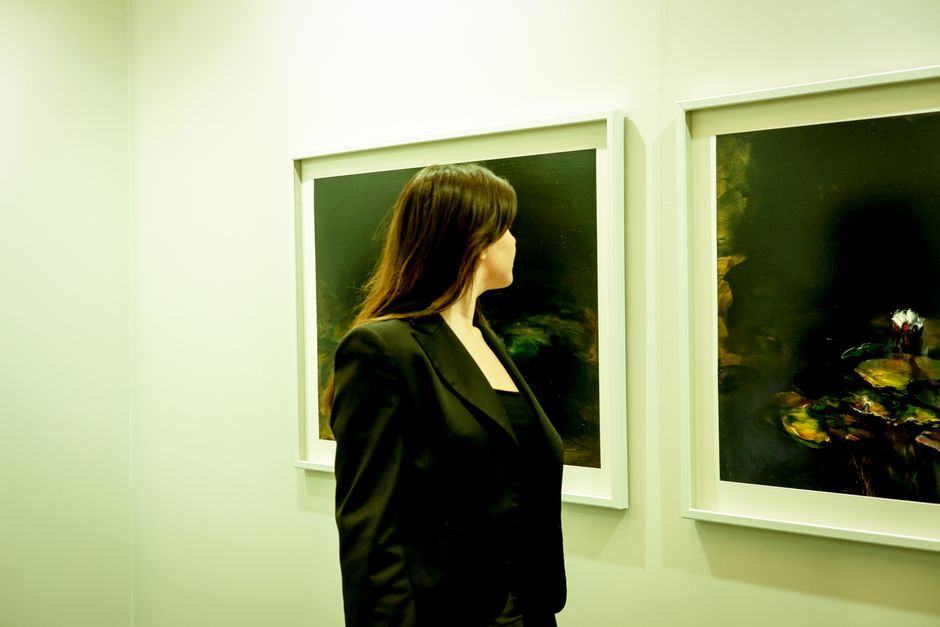 Cultura São Paulo — A woman in a black suit examines paintings in a modern gallery setting.