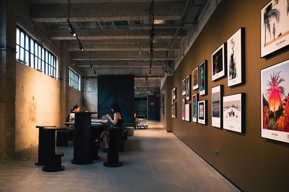 Cultura São Paulo — Art gallery hallway with framed artworks and visitors seated inside, under warm lighting.